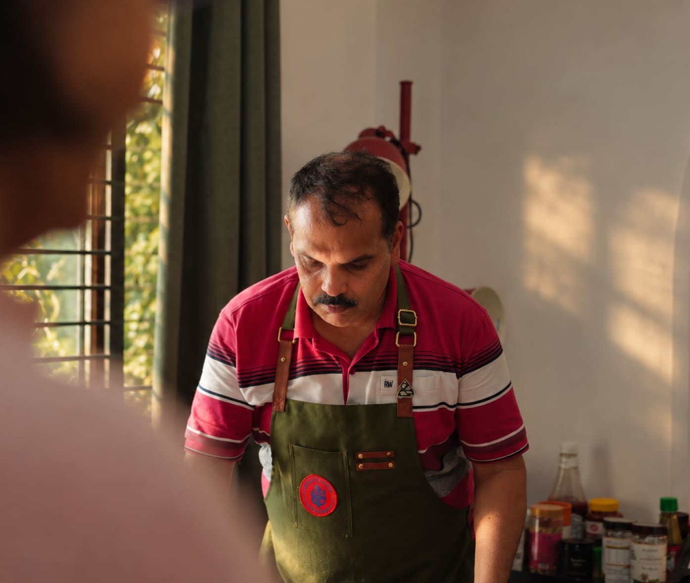 Dannes in a striped shirt and green apron at work in the kitchen