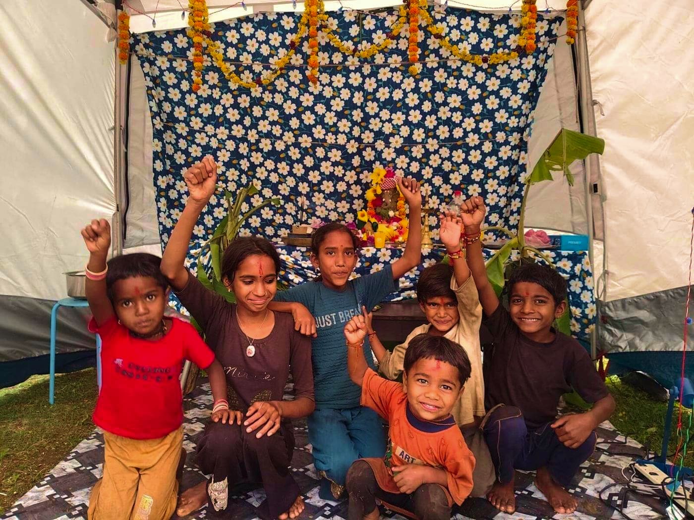 Children cheering in front of the Ganpati shrine, under marigold garlands