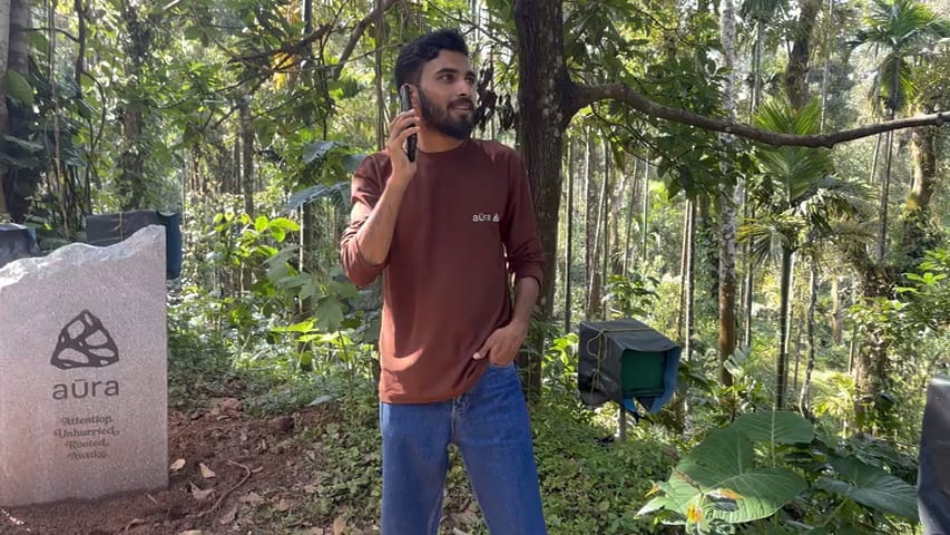 Deepak on the phone beside the Aura stone marker, deep in the trees