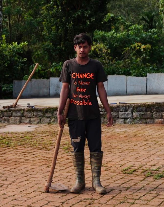 A young man in gumboots leaning on a hoe, his T-shirt reading Change is never easy but always possible