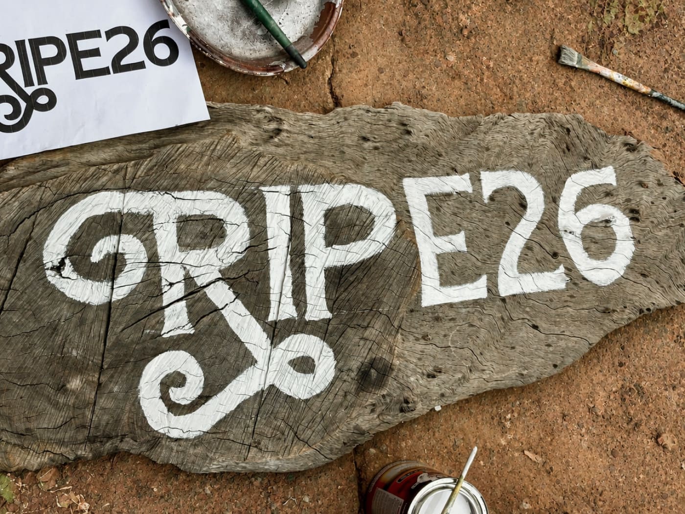 RIPE26 being painted in white on a slice of wood, brushes and paint beside it