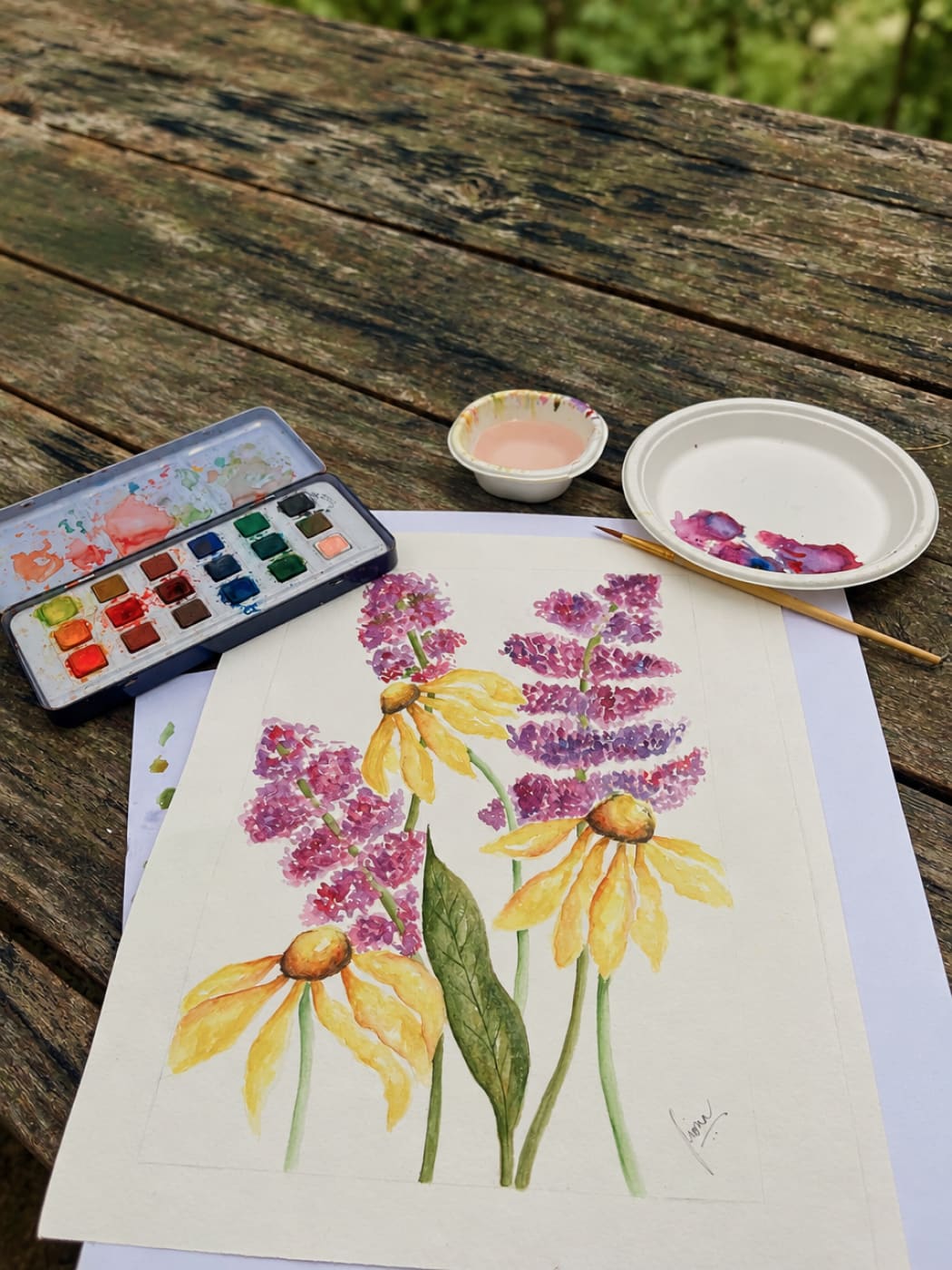 A watercolour of yellow and purple flowers beside a paint box