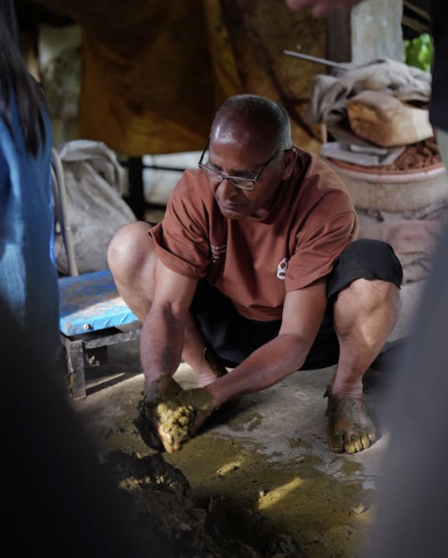 A man crouched barefoot, working the compost with his hands