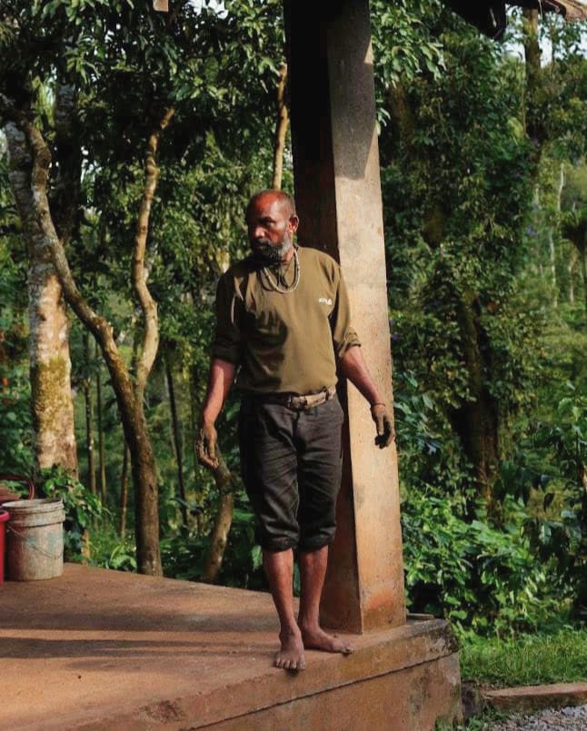 A man standing barefoot under the eaves, the forest behind