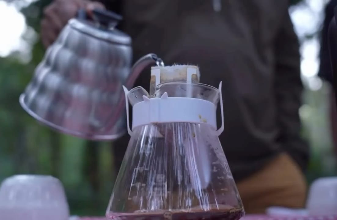 Hot water poured from a kettle into a paper dripper over a glass server