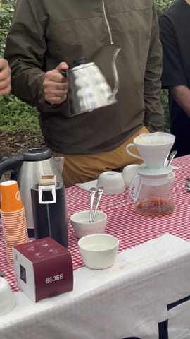 Pouring hot water over a pour-over dripper at the checked tasting table