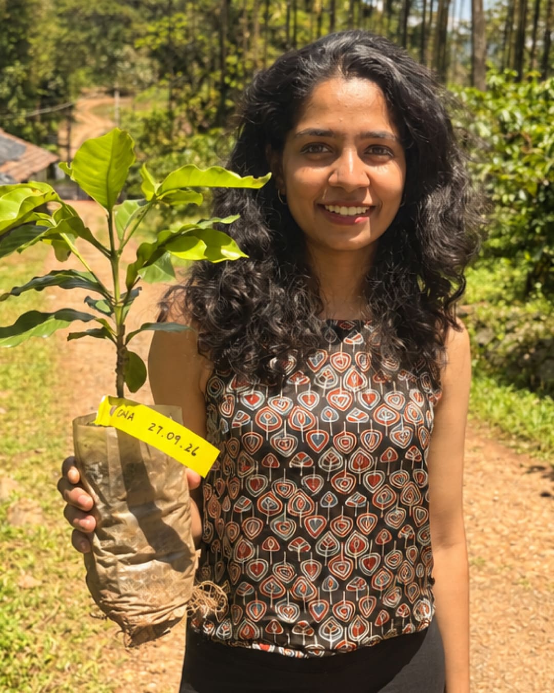 A smiling guest holding up a coffee sapling, its tag marked with a name and the date