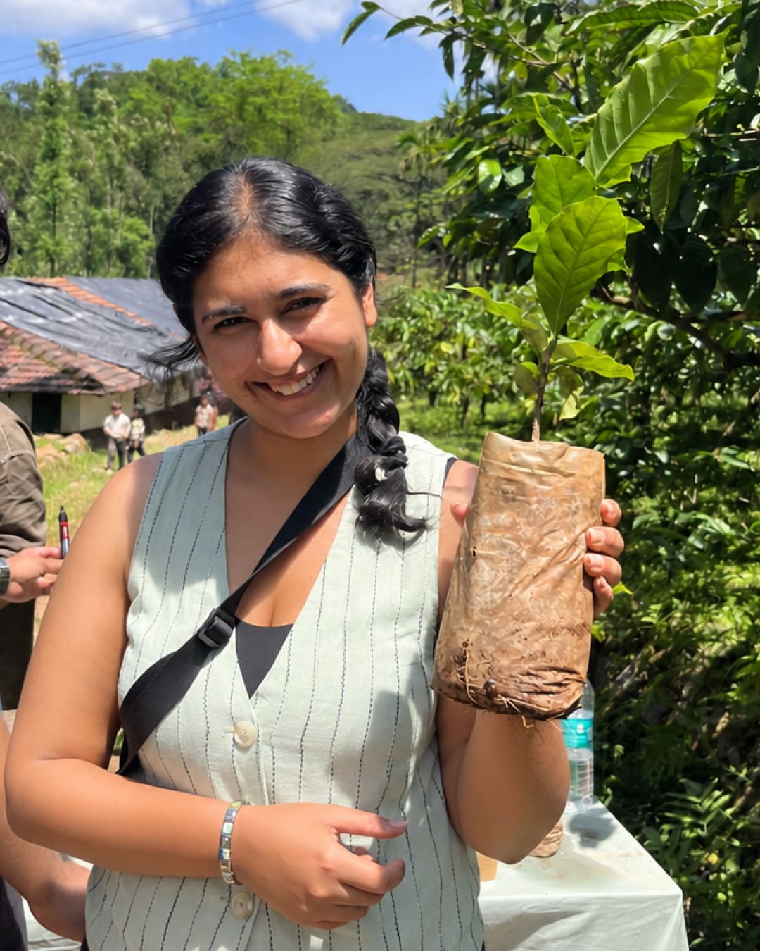 A smiling guest in a striped waistcoat holding a coffee sapling in its paper sleeve