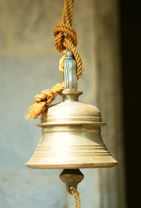 A brass bell hanging on a rope by the house