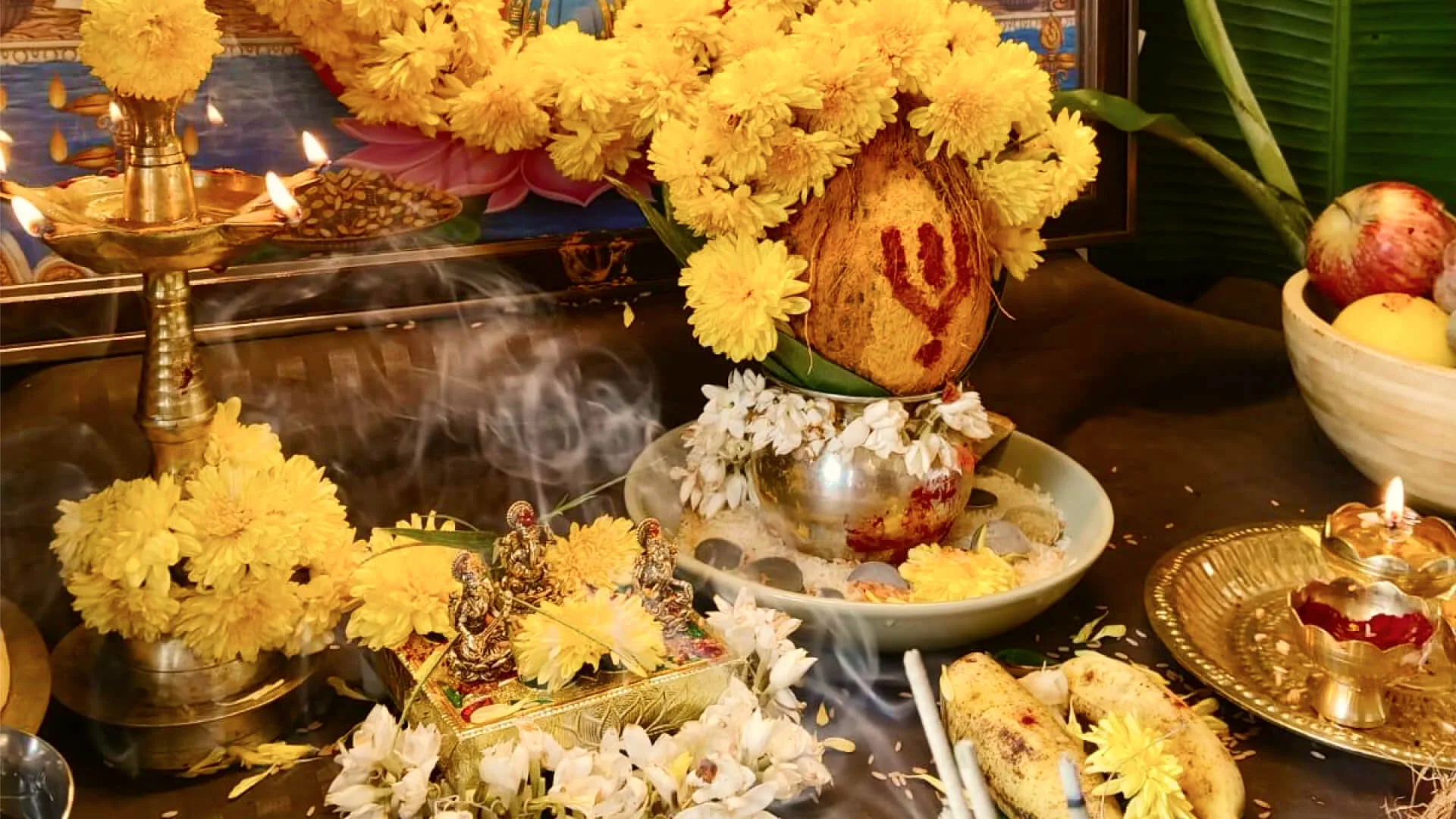 A pooja laid out with marigolds, brass lamps, a garlanded coconut and incense smoke