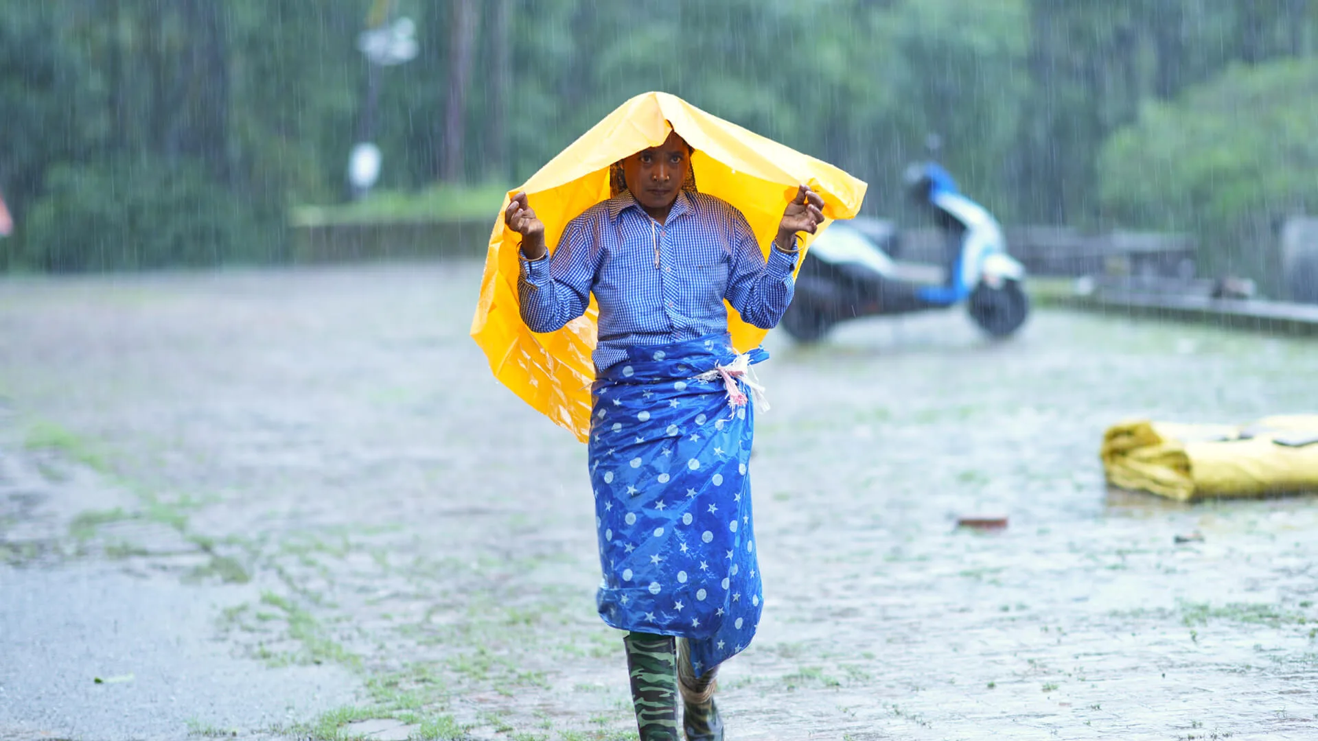Someone crossing open ground in heavy rain under a sheet